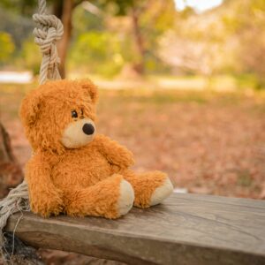 Adorable teddy bear resting on a wooden swing in a serene park setting, perfect for childhood memories.